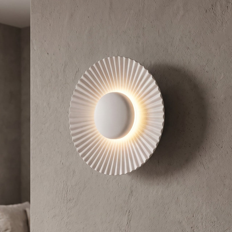 Applique murale LED moderne en aluminium blanc mat, 16 cm de diamètre, offrant une lumière chaleureuse et un design plissé élégant pour un salon.