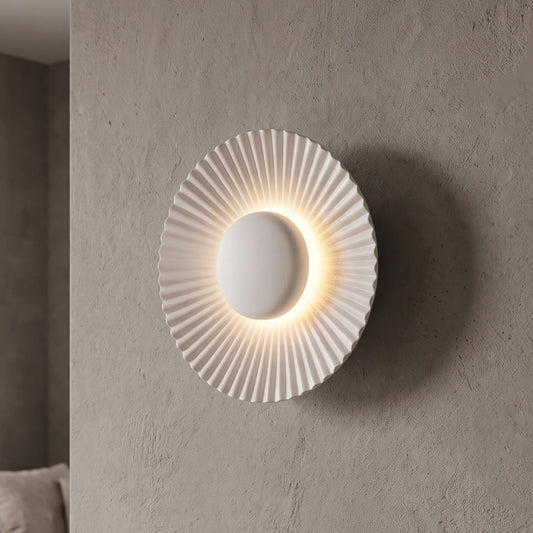 Applique murale LED moderne en aluminium blanc mat, 16 cm de diamètre, offrant une lumière chaleureuse et un design plissé élégant pour un salon.