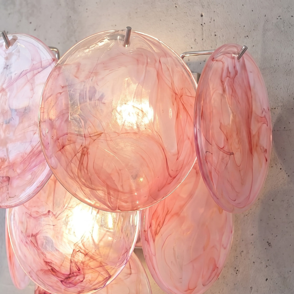 Détail rapproché des disques de verre teinté rose ambré de l'applique, révélant les motifs tourbillonnants uniques et la richesse de la matière.
