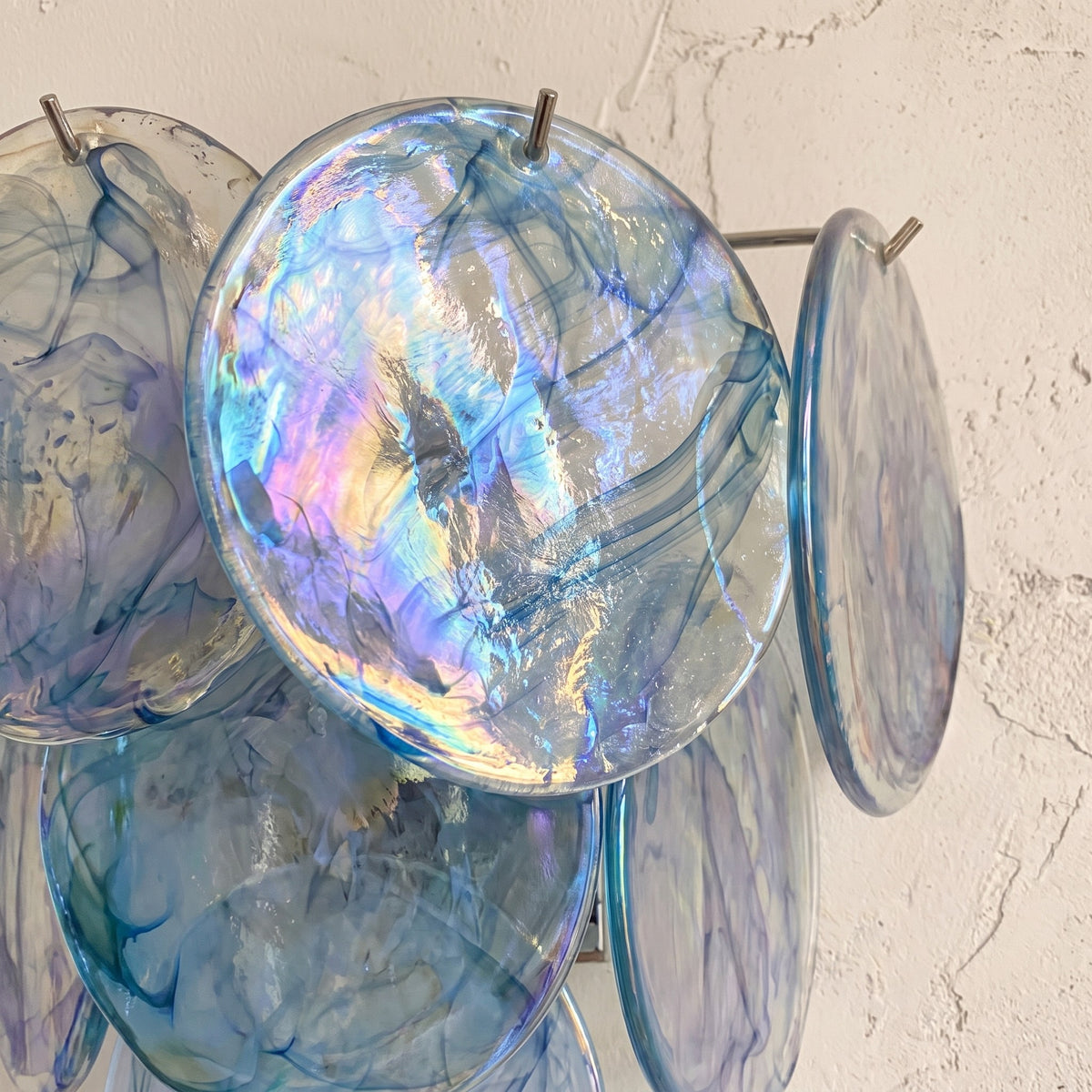 Vue détaillée d'une applique murale style Murano en verre bleu, montrant les nuances irisées et la texture unique des disques.