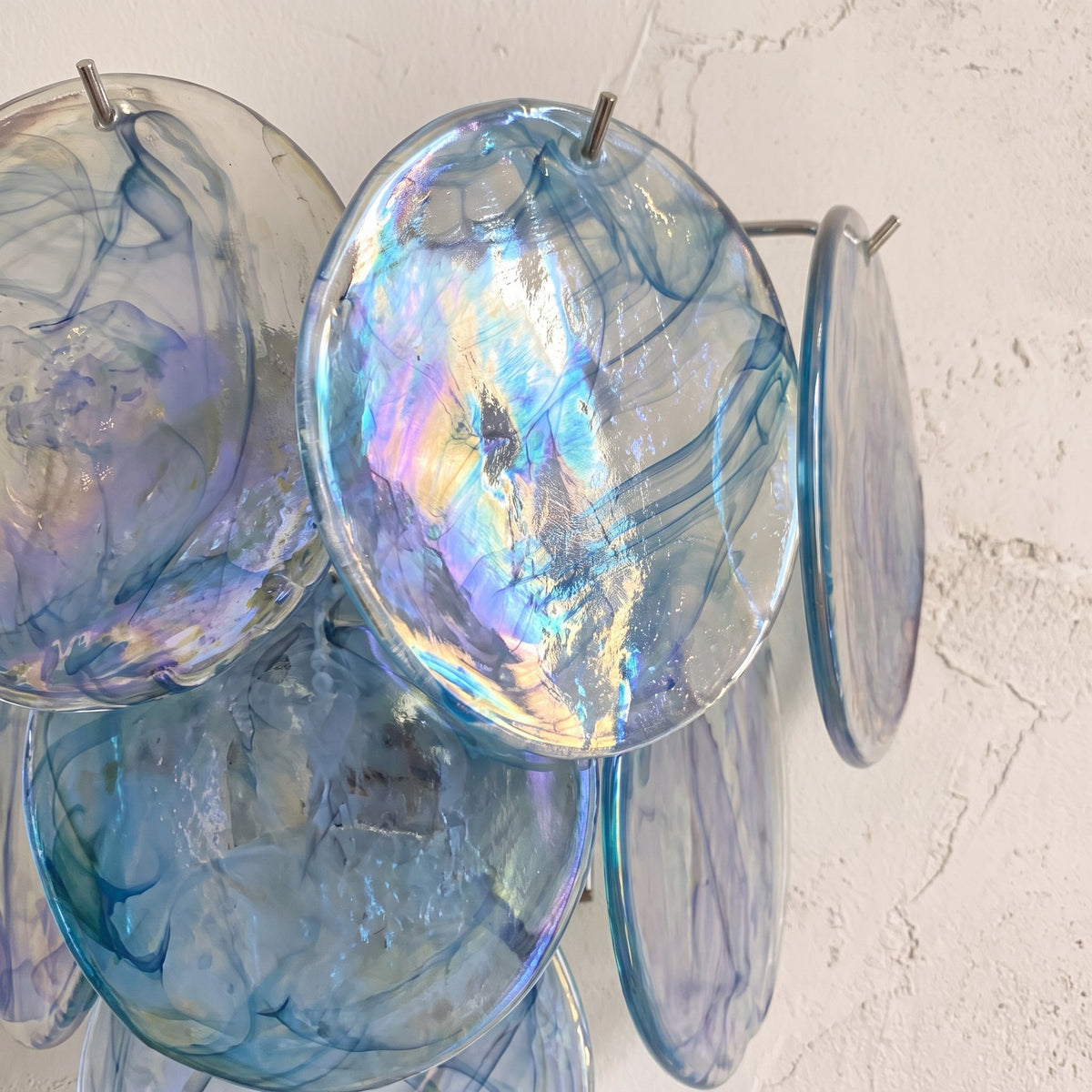 Gros plan sur les disques de verre soufflé de l'applique murale bleue, révélant la complexité et la beauté de chaque pièce.