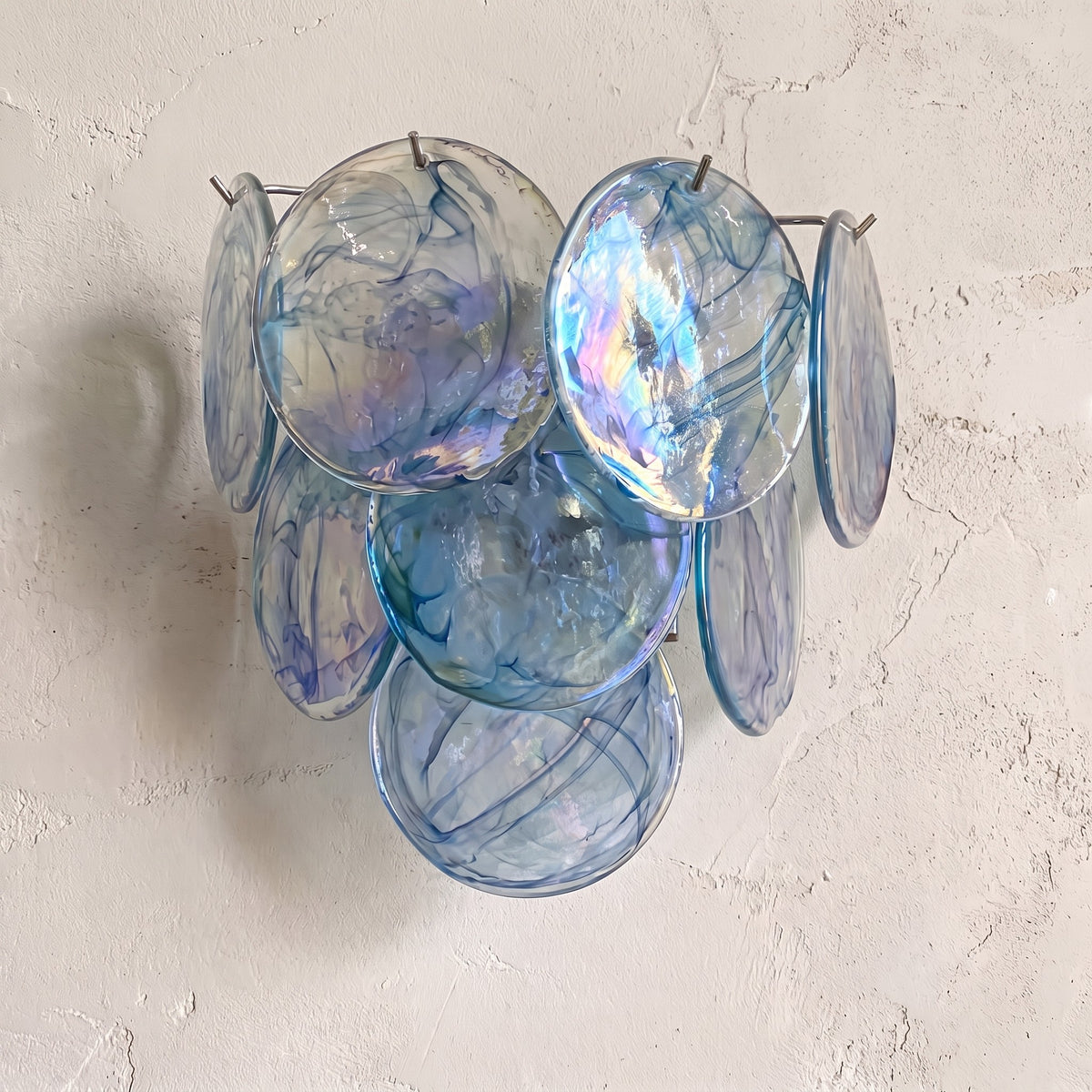 Applique murale style Murano vintage bleue, composée de disques de verre irisés, éclairant un salon moderne avec élégance.