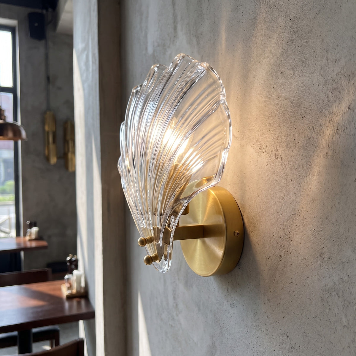 Applique murale design avec abat-jour en verre transparent et support doré, créant un point focal élégant au-dessus d'un meuble bas dans une chambre.