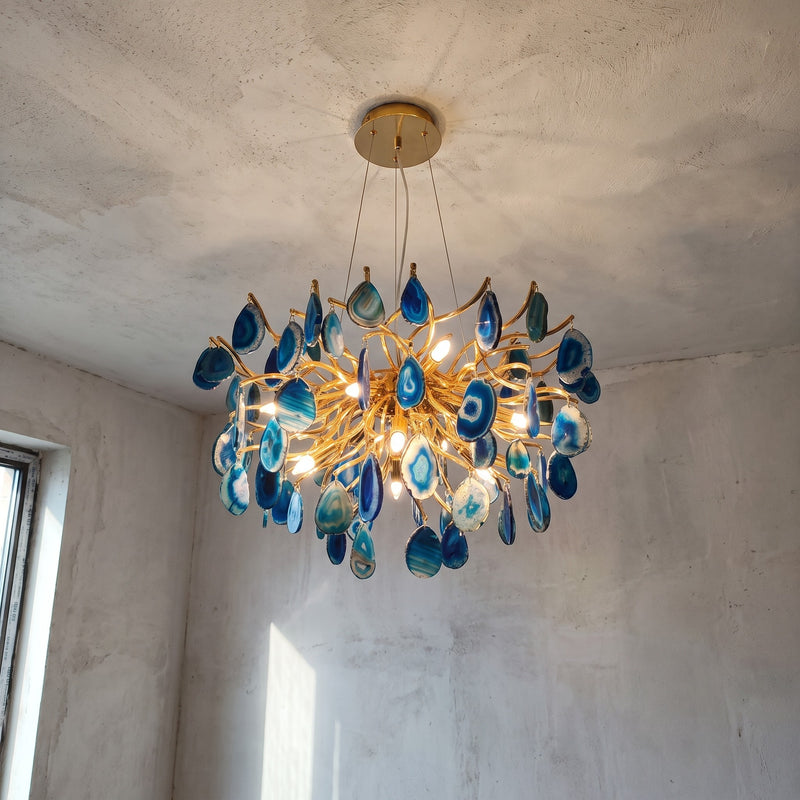 Lustre design en agate bleue et métal doré brillant, vu de face, illuminant un intérieur moderne avec élégance.