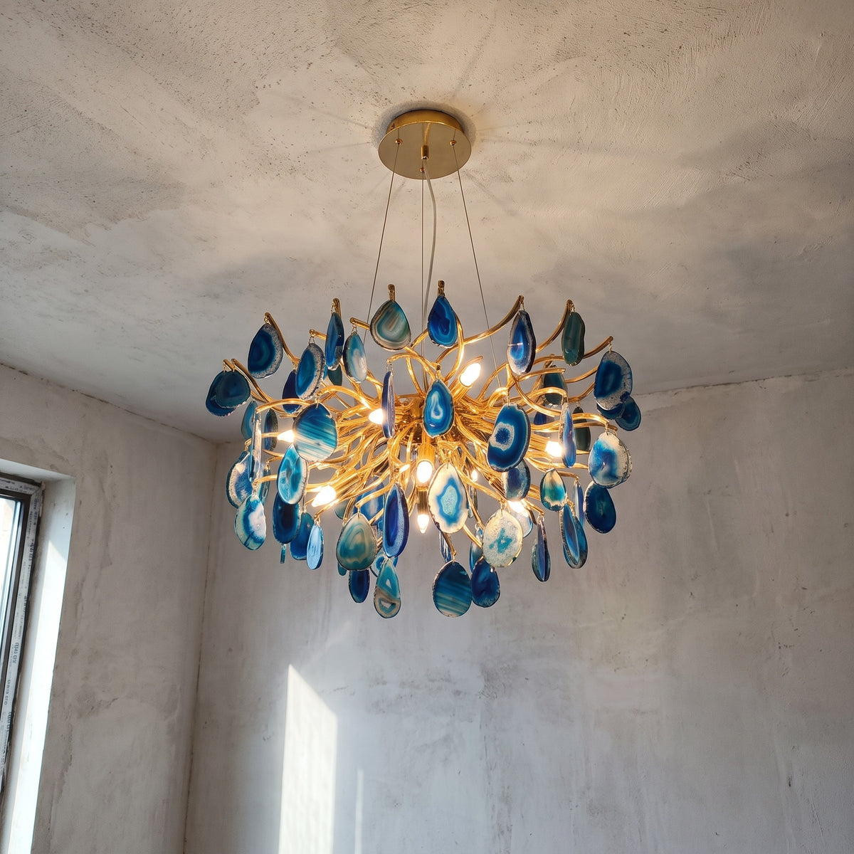 Lustre design en agate bleue et métal doré brillant, vu de face, illuminant un intérieur moderne avec élégance.