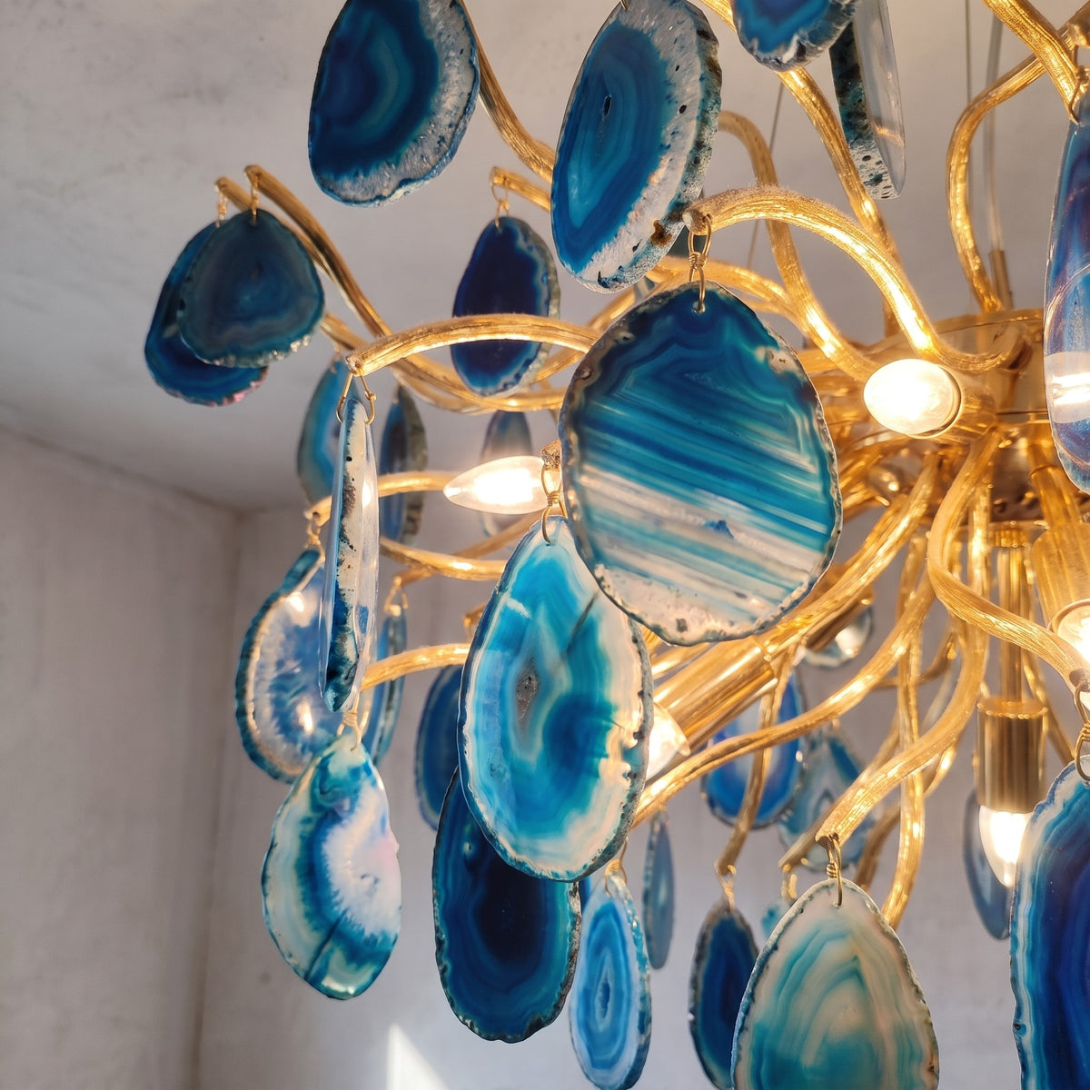 Vue latérale du luminaire suspendu, montrant la profondeur et la texture des agates bleues et du cadre doré luxueux.