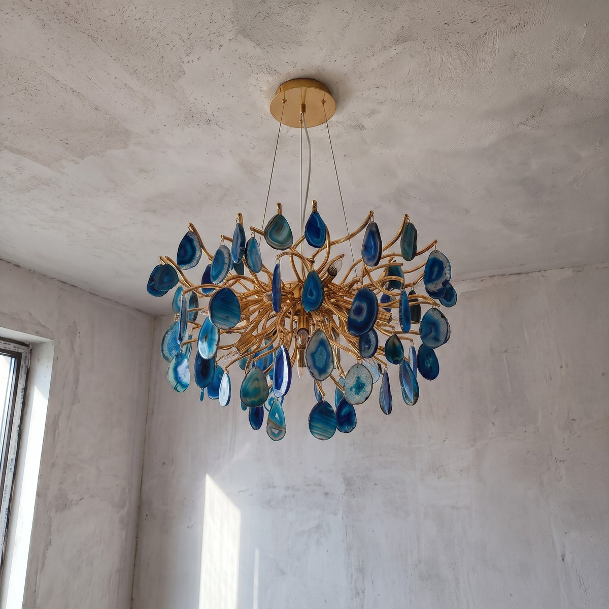 Détail rapproché des tranches d'agate bleue naturelle, suspendues à la structure en métal doré du lustre contemporain.