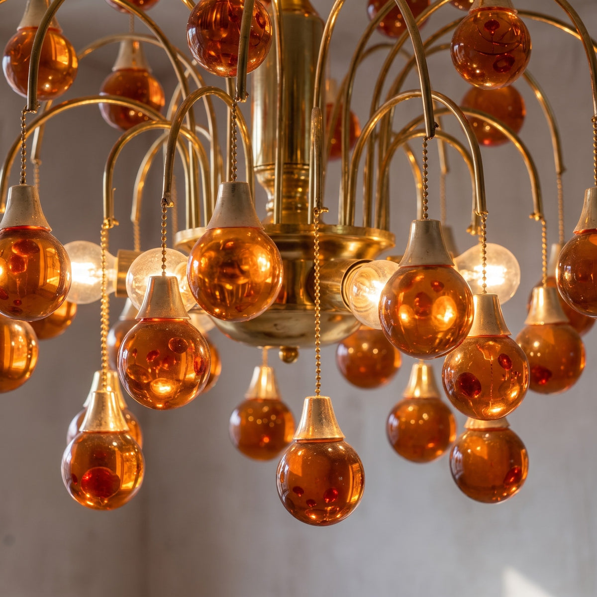 Lustre style Art Déco allumé, mettant en valeur l'éclat chaleureux des pampilles en verre orange ambré et la brillance de sa finition dorée.