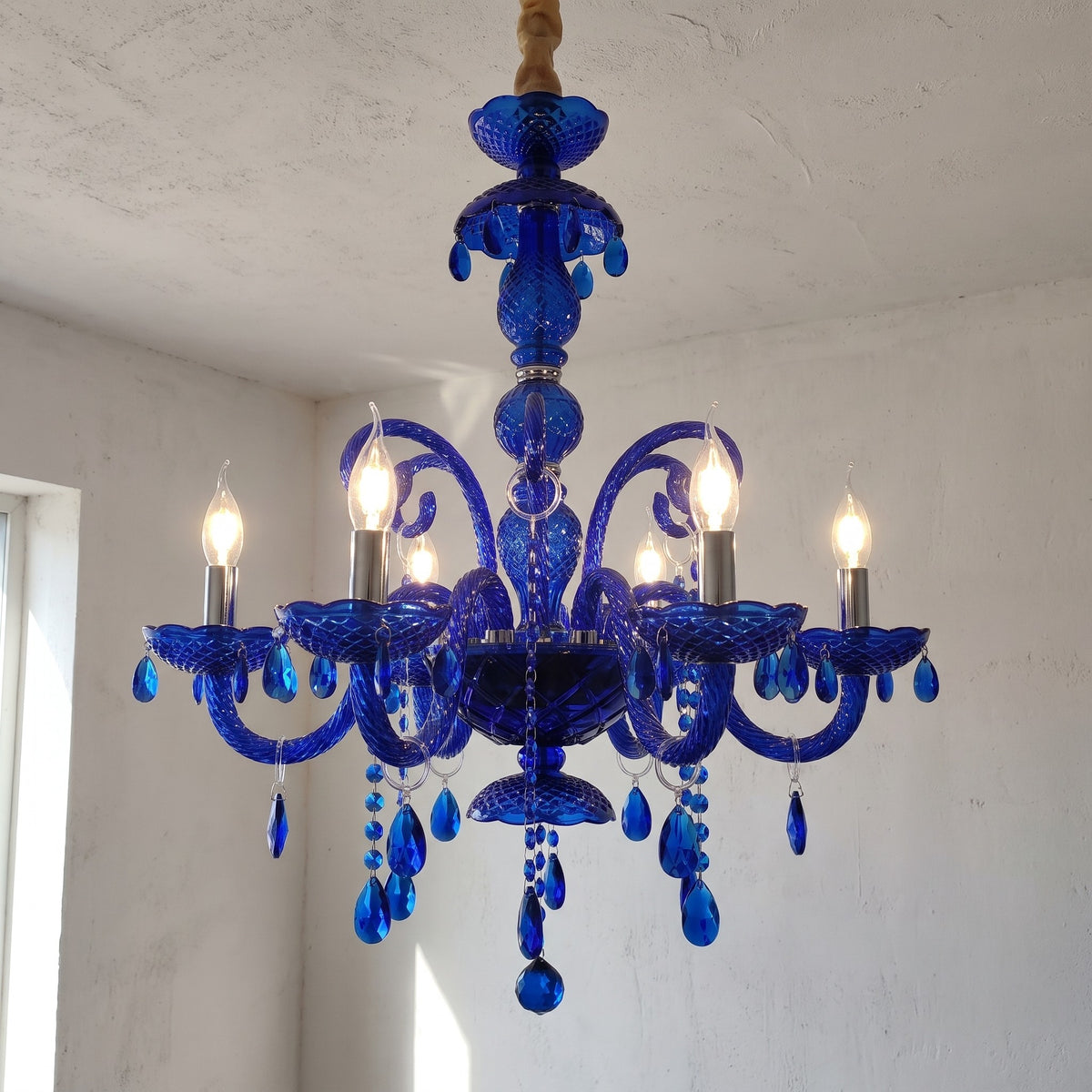 Lustre bleu saphir style Murano, design moderne, éclairant un grand salon avec élégance et une lumière chaleureuse.