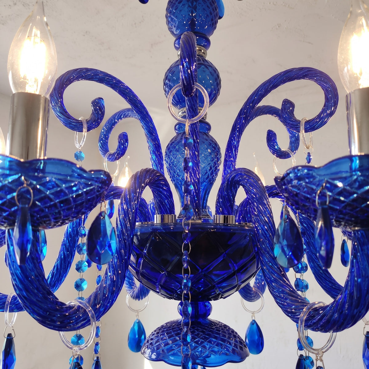 Détail du lustre en cristal poli bleu saphir, mettant en valeur les bras courbés et les pendentifs brillants.