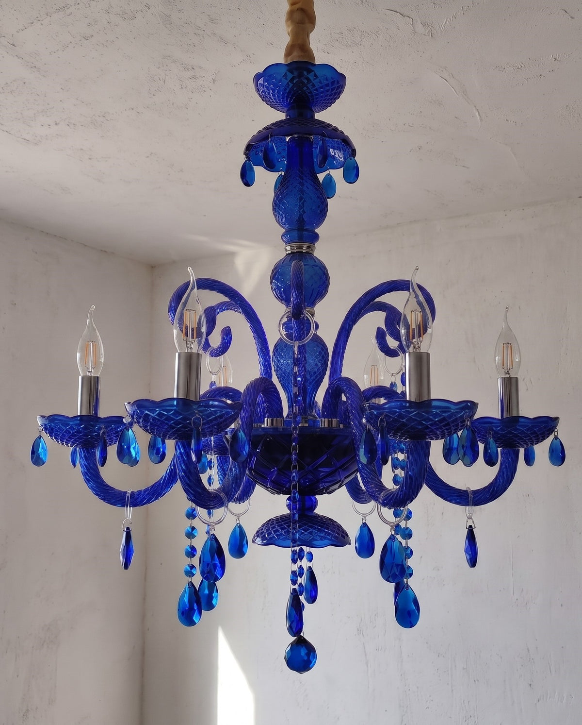 Le lustre bleu saphir allumé, diffusant une lumière douce à travers ses ornements en cristal dans une ambiance raffinée.