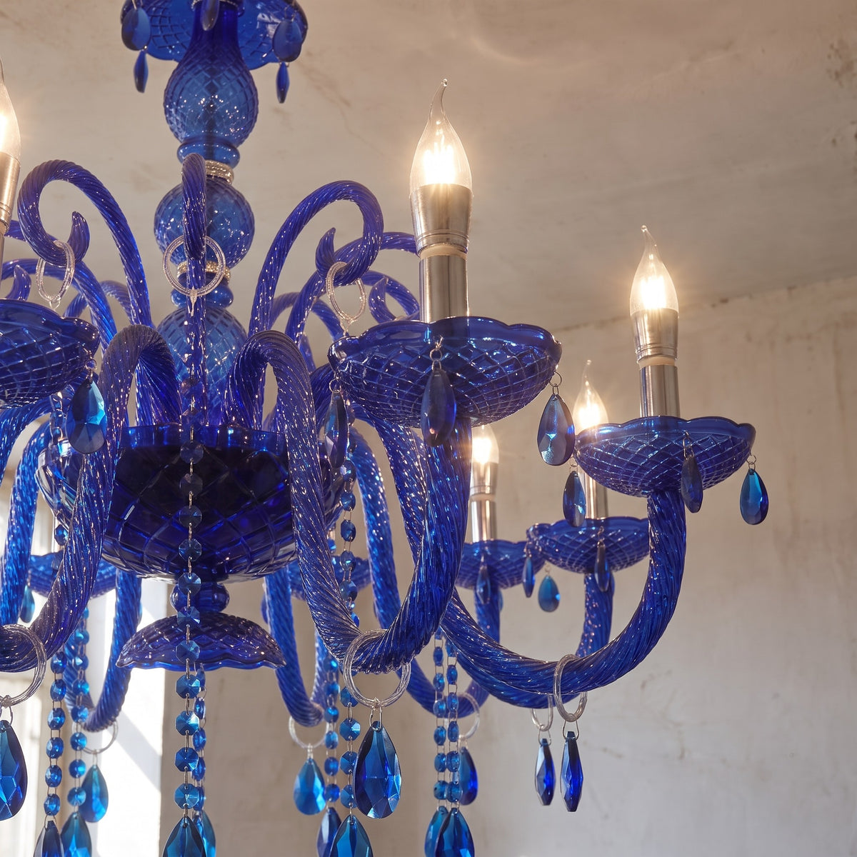 Vue rapprochée des bras courbés et des pampilles en cristal bleu saphir d'un lustre vénitien, illuminant la pièce.