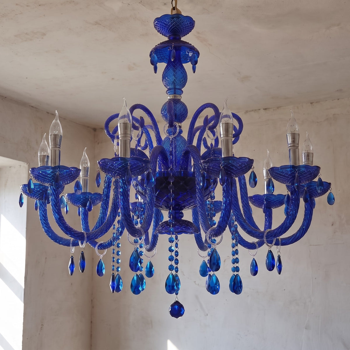 Le lustre style Murano bleu saphir allumé, diffusant une lumière chaleureuse et accentuant les reflets du cristal.