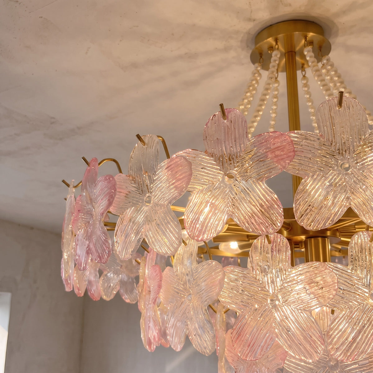 Détail rapproché des pétales de verre rose pâle du lustre, reflétant la lumière avec une délicatesse artistique.