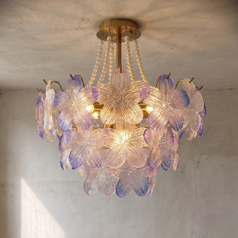 Lustre suspension floral en verre irisé aux reflets lavande, éclairant un salon avec une lumière douce et une ambiance romantique. Dimensions 60x52cm.