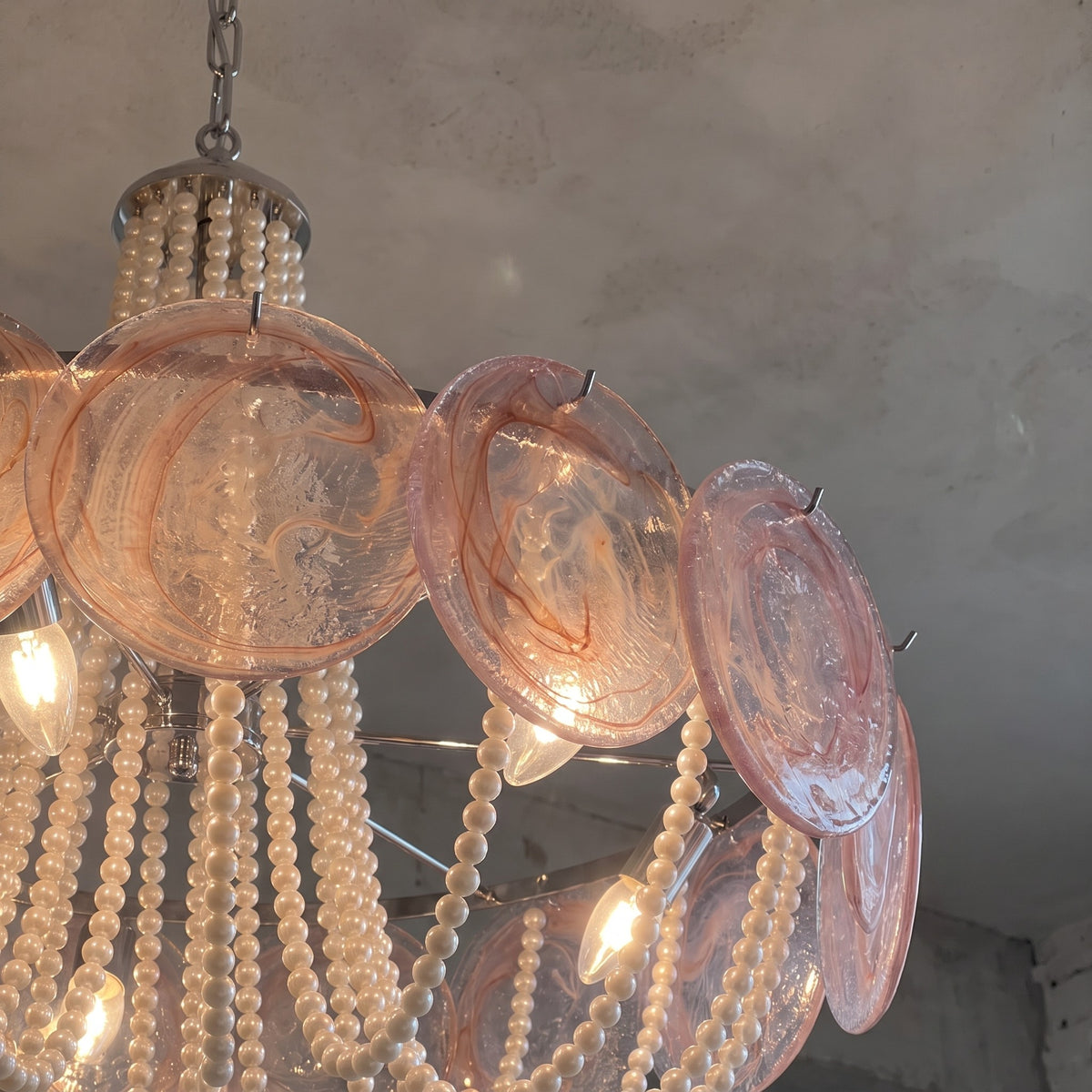 Vue rapprochée des disques de verre style Murano, présentant des motifs subtils et une teinte rose délicate pour ce lustre.