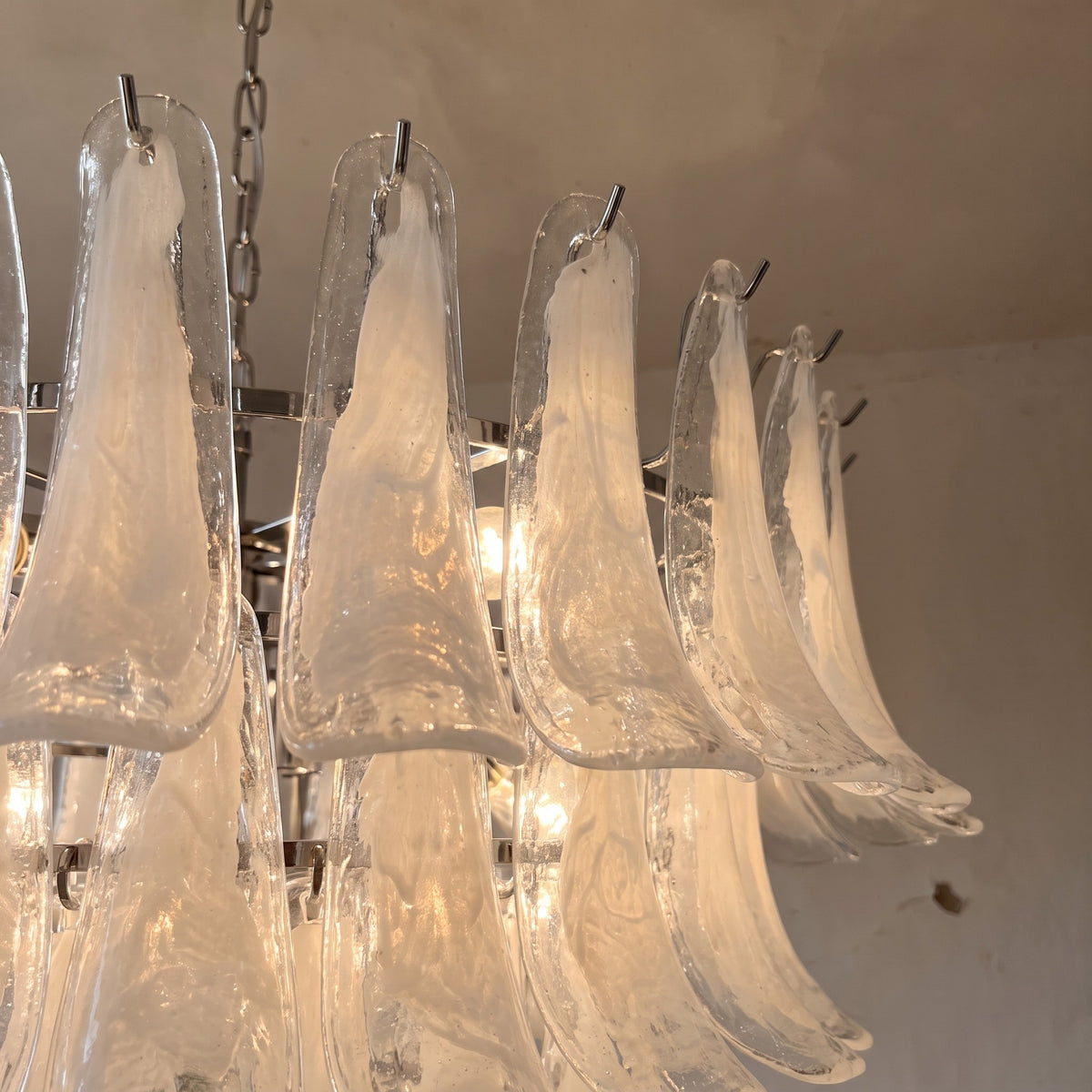 Perspective du lustre blanc opalescent vu d'en bas, accentuant sa grandeur et la complexité de son design lumineux.