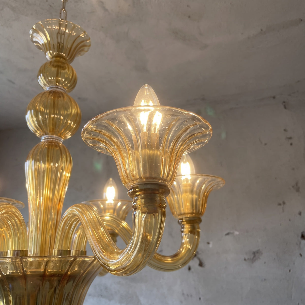 Lustre en verre teinté caramel, inspiré du design Murano, suspendu majestueusement dans une chambre principale sophistiquée.