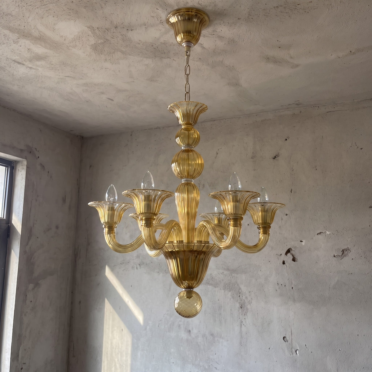 Installation d'un lustre style Murano caramel, montrant la qualité du verre et la structure métallique délicate.