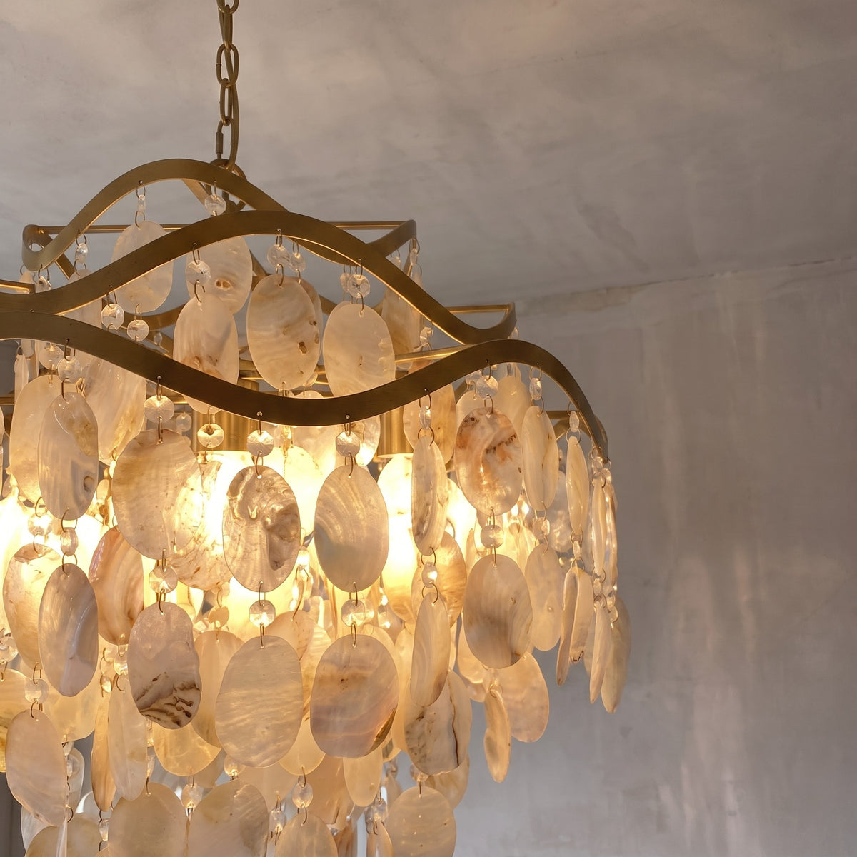 Gros plan sur la structure dorée du lustre, mettant en valeur la finition plaquée et l'assemblage artistique des éléments de nacre naturelle.