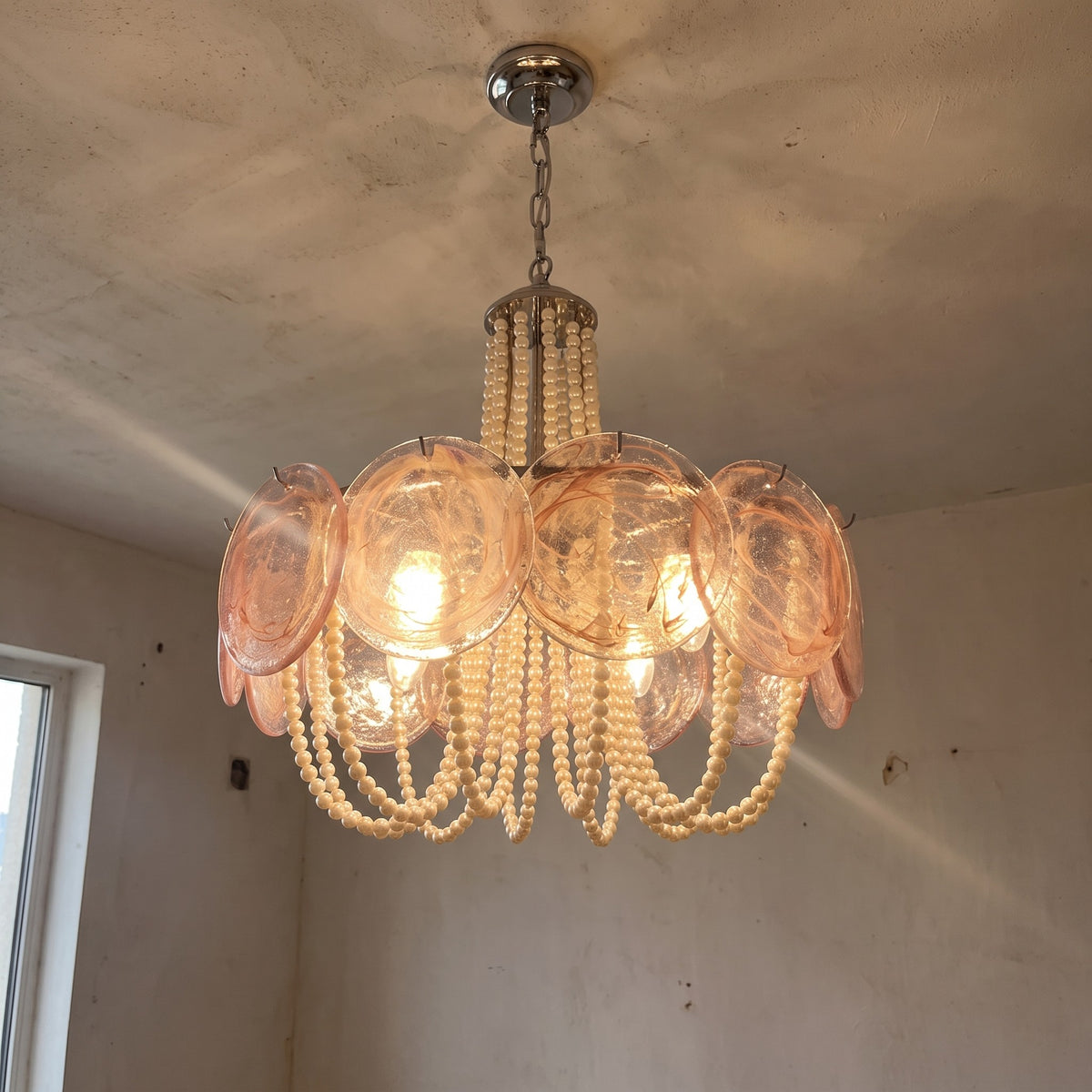Lustre rond style Murano rose poudré et perles nacrées, suspendu au plafond, illuminant un salon moderne avec élégance.