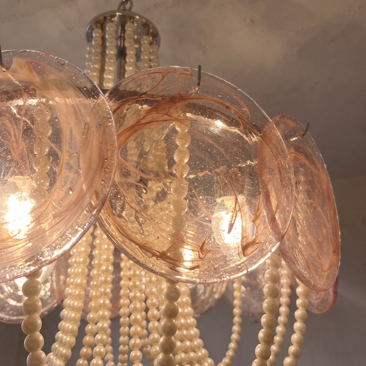Détail des guirlandes de perles couleur crème pendant sous le lustre, ajoutant une touche de raffinement et de brillance.
