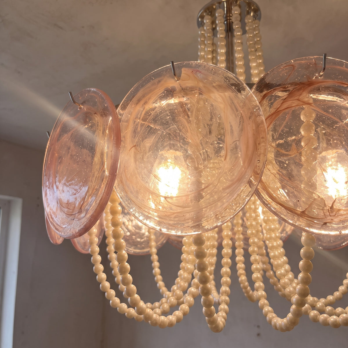 Vue rapprochée des éléments en verre rose poudré du lustre, révélant la texture unique et les reflets délicats de la lumière.
