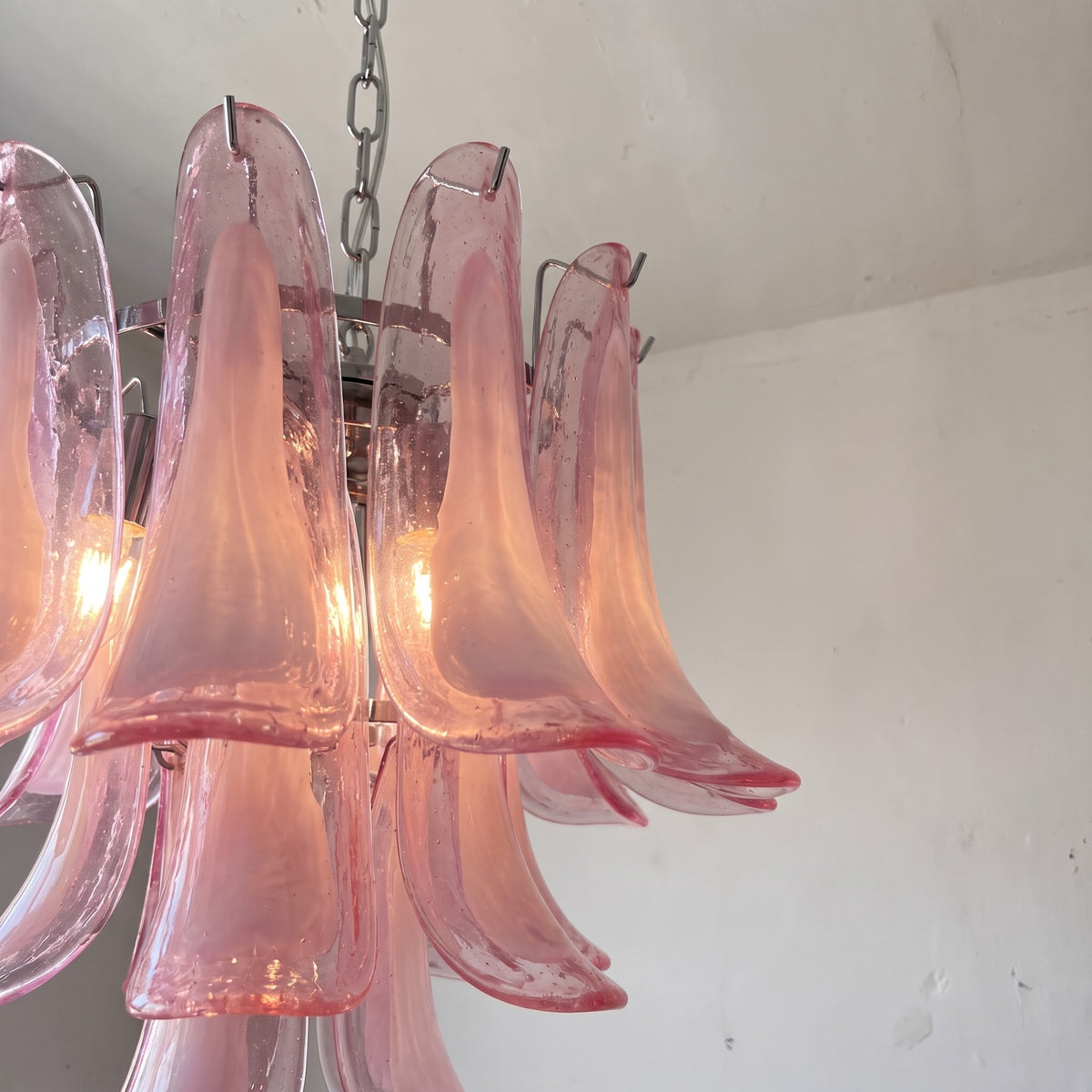 Image du lustre éteint, montrant la structure en métal chromé poli et les multiples couches de verre rose translucide.