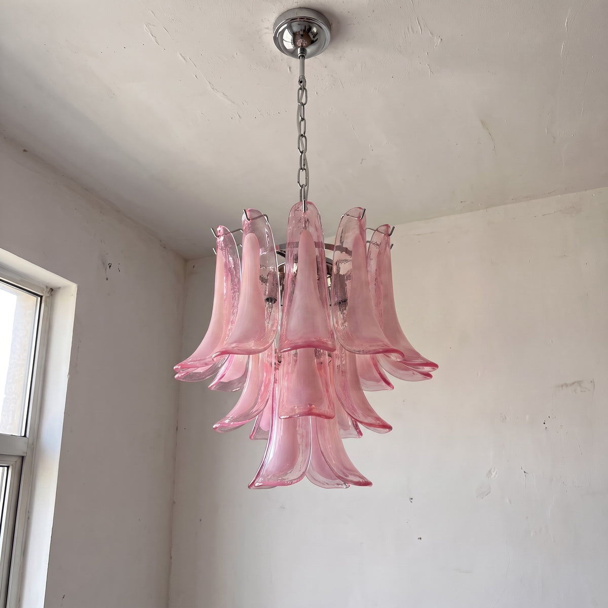 Lustre style Art Déco avec ses formes de pétales organiques en verre rose, suspendu au plafond, ajoutant une dimension artistique.