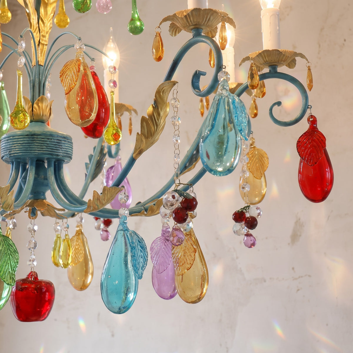 Lustre allumé diffusant une lumière chaude, mettant en valeur la transparence et les reflets des ornements en verre coloré dans une pièce élégante.