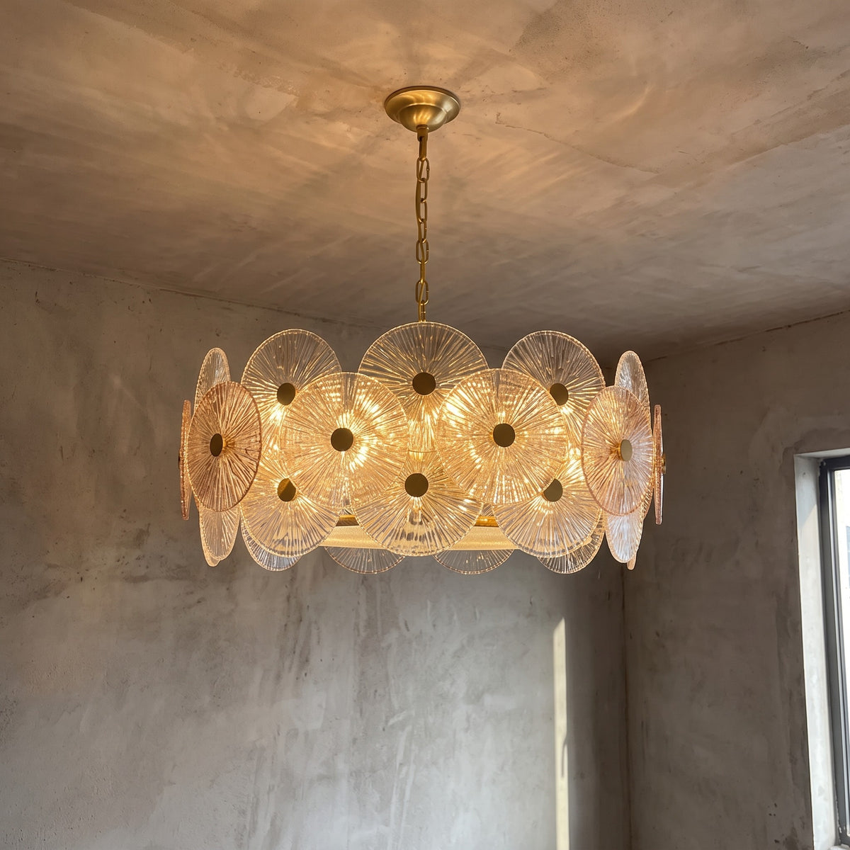 Lustre rond style Murano en verre ambré et acier inoxydable doré, allumé, éclairant un salon élégant.