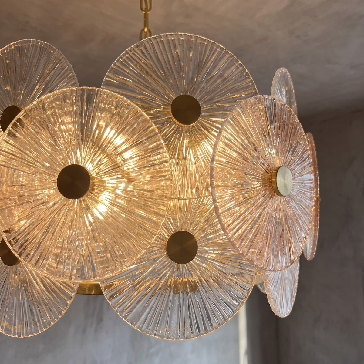 Détail des disques de verre texturé ambré du lustre, montrant les reflets de lumière et le cadre doré.