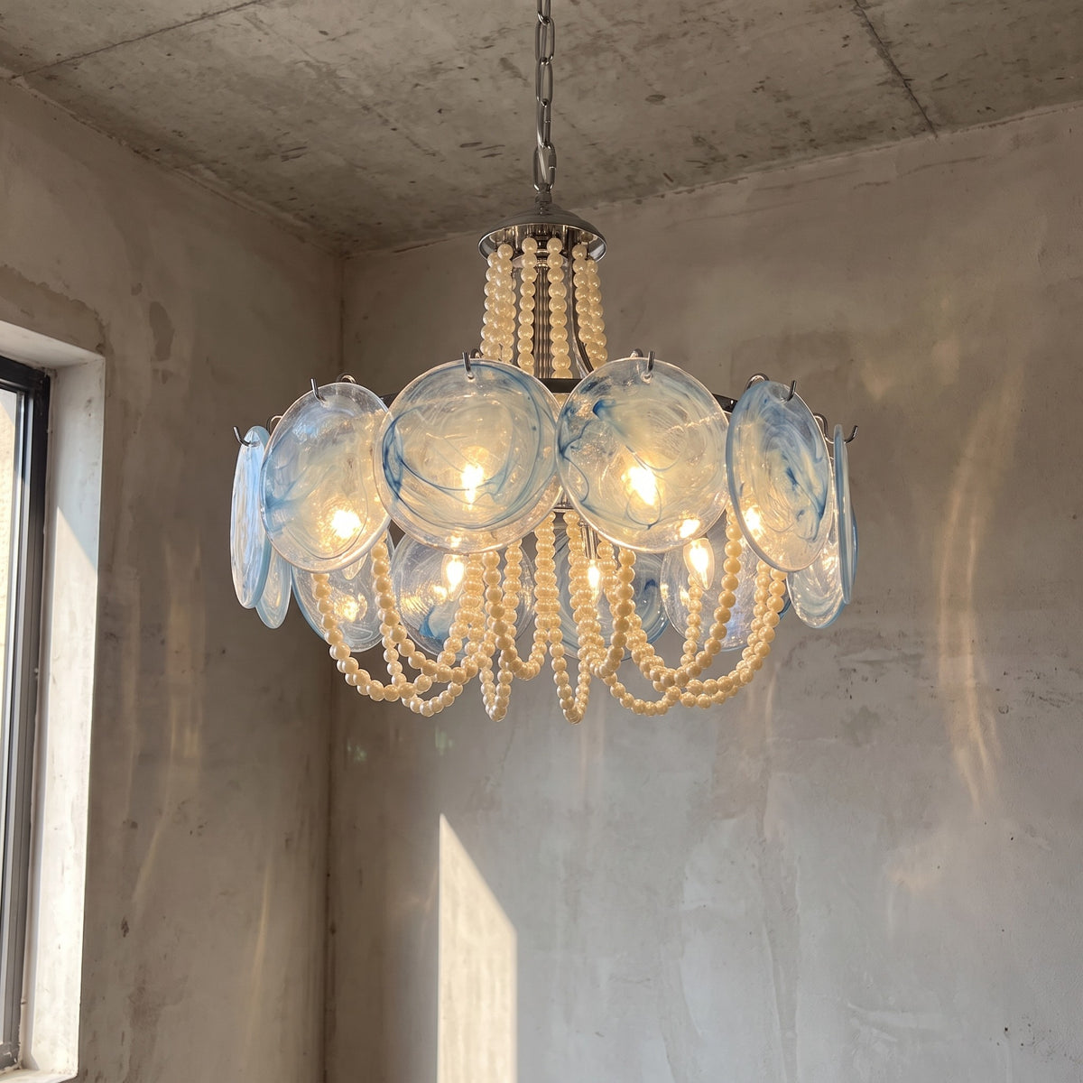 Lustre rond style Murano en verre bleu-vert et perles crème, diffusant une lumière élégante dans un salon moderne.