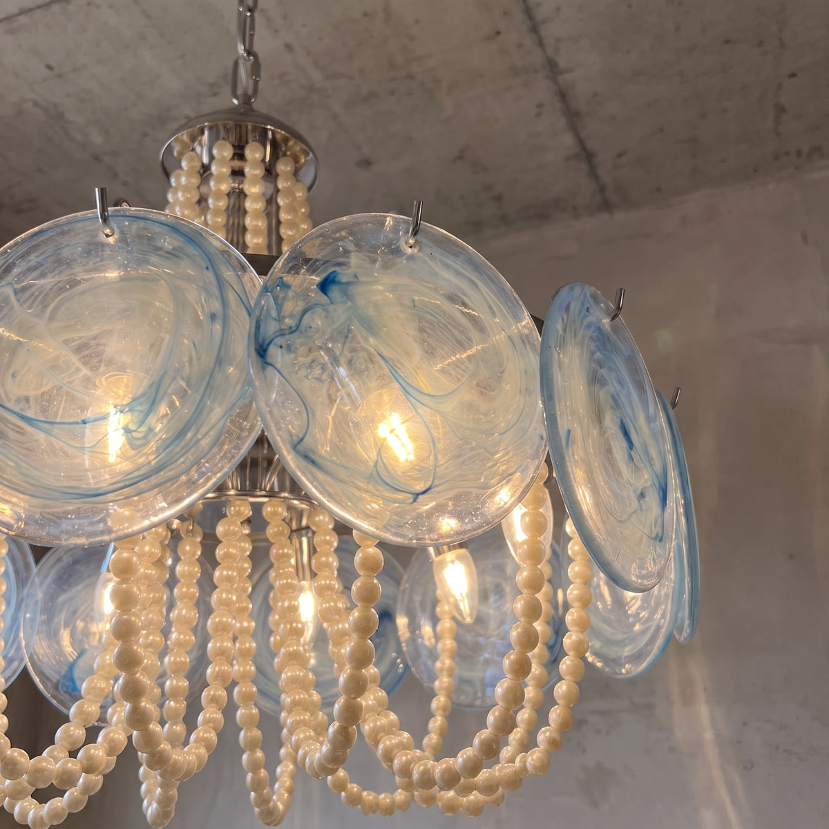 Lustre suspension avec chaînes de perles couleur crème, éclairant harmonieusement une salle à manger intemporelle.