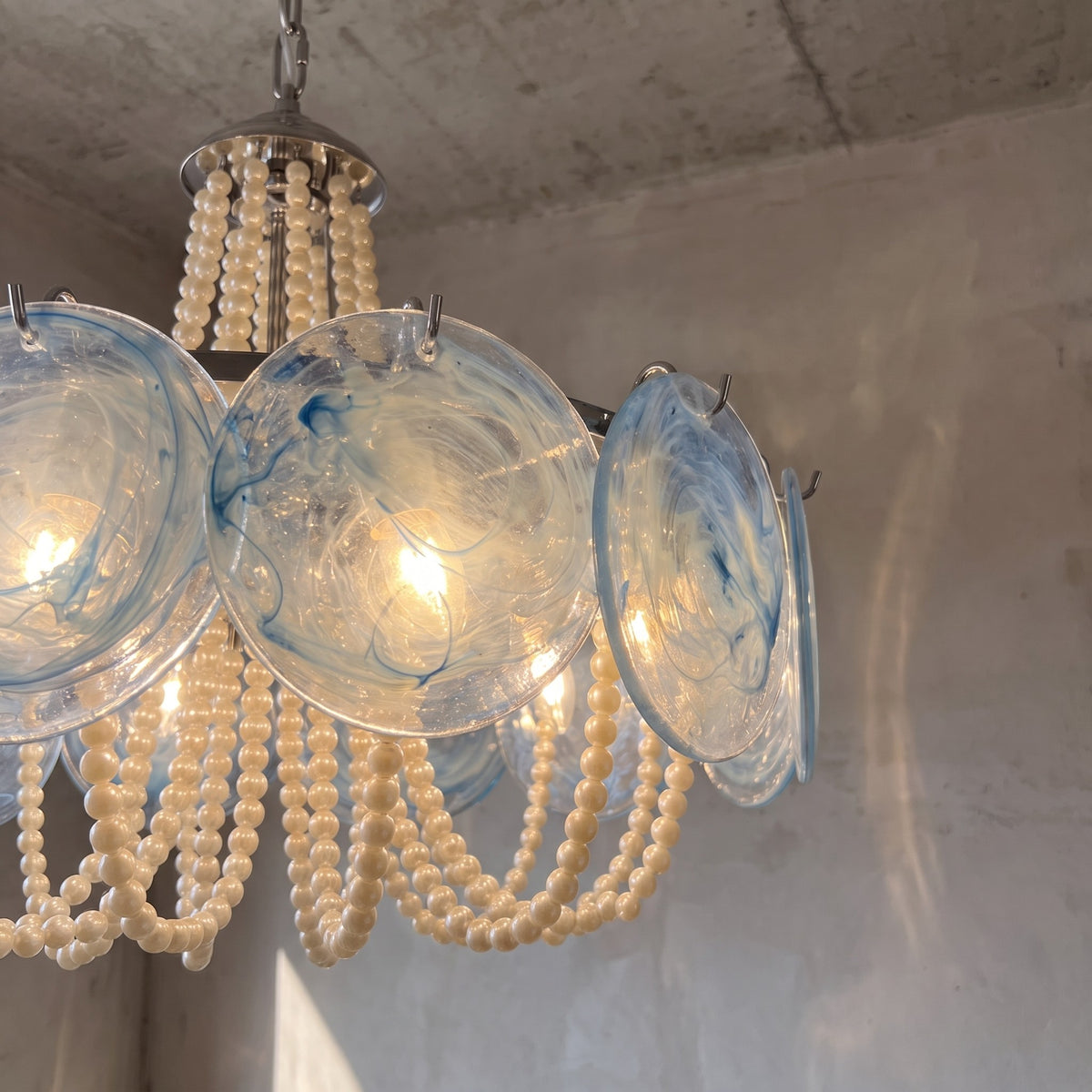 Détail de la structure en acier poli du lustre, supportant les éléments en verre et les guirlandes de perles.