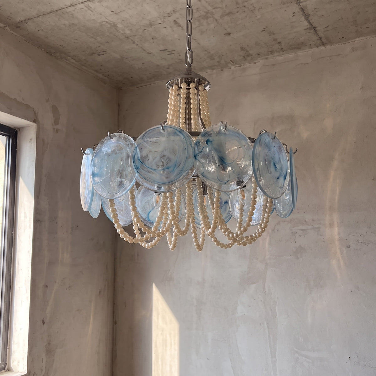 Le lustre allumé, révélant les reflets doux et chaleureux du verre bleu-vert et des perles dans la pièce.