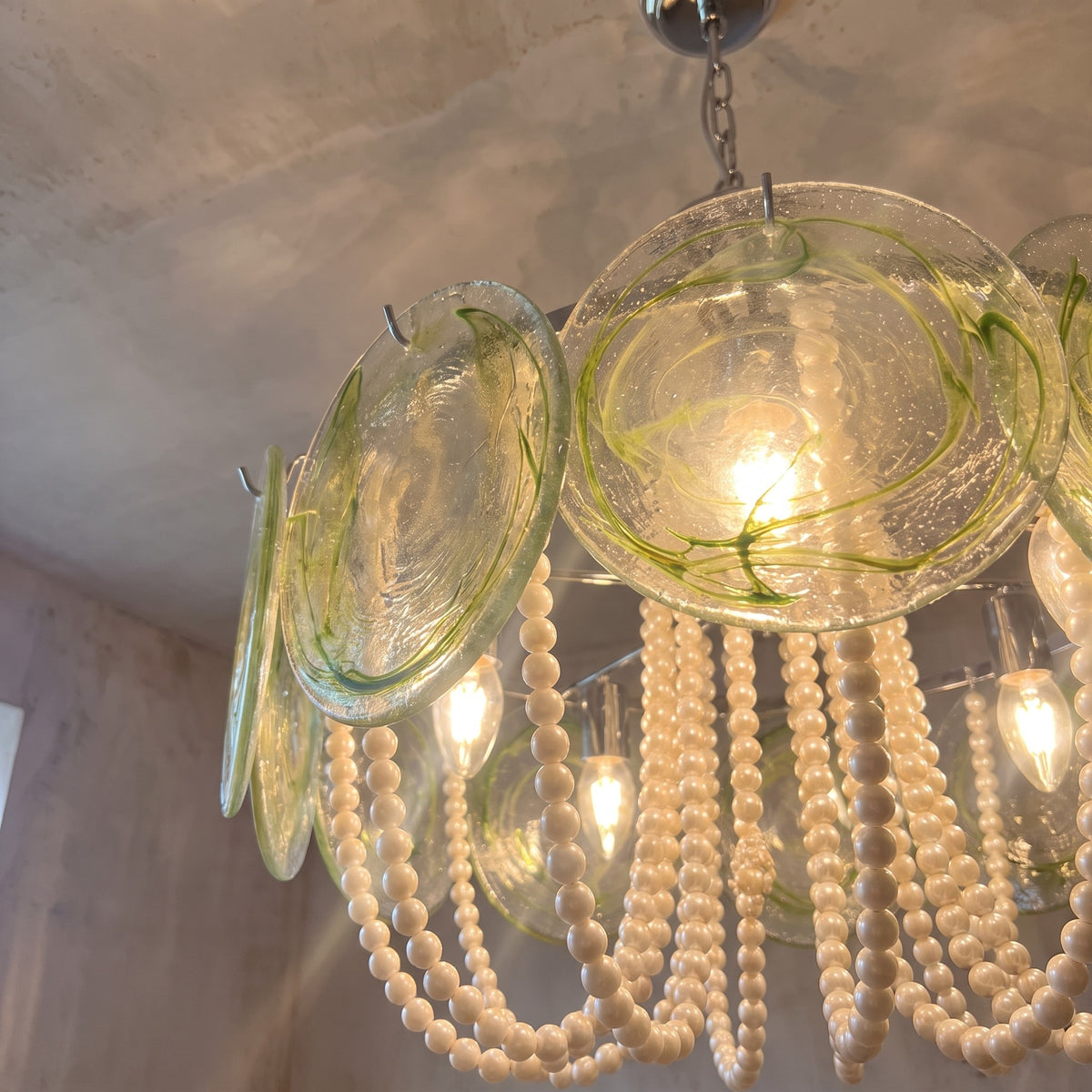 Détail des disques de verre soufflé aux reflets vert clair et dorés, capturant la lumière pour une ambiance unique.