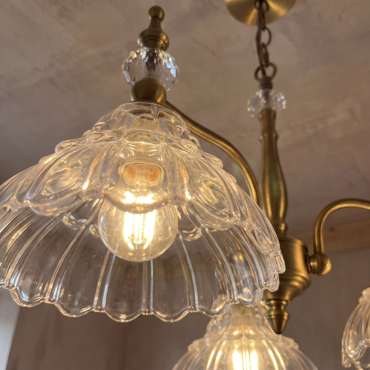 Détail des abat-jour en verre transparent cannelé du lustre, mettant en valeur la finesse de sa texture et son éclat délicat.