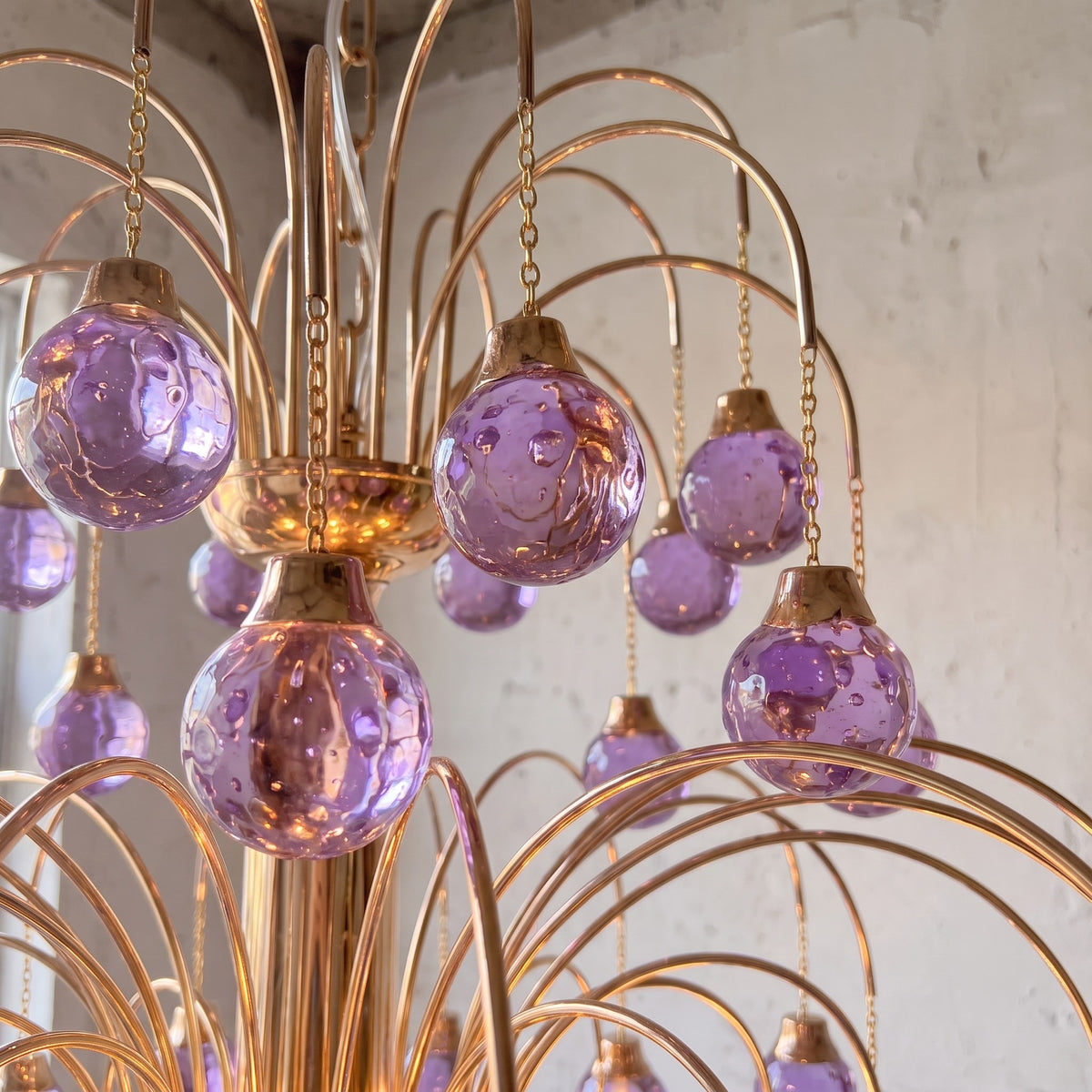 Détail rapproché du lustre Art Déco, montrant les perles en verre soufflé violet et la structure en métal doré.
