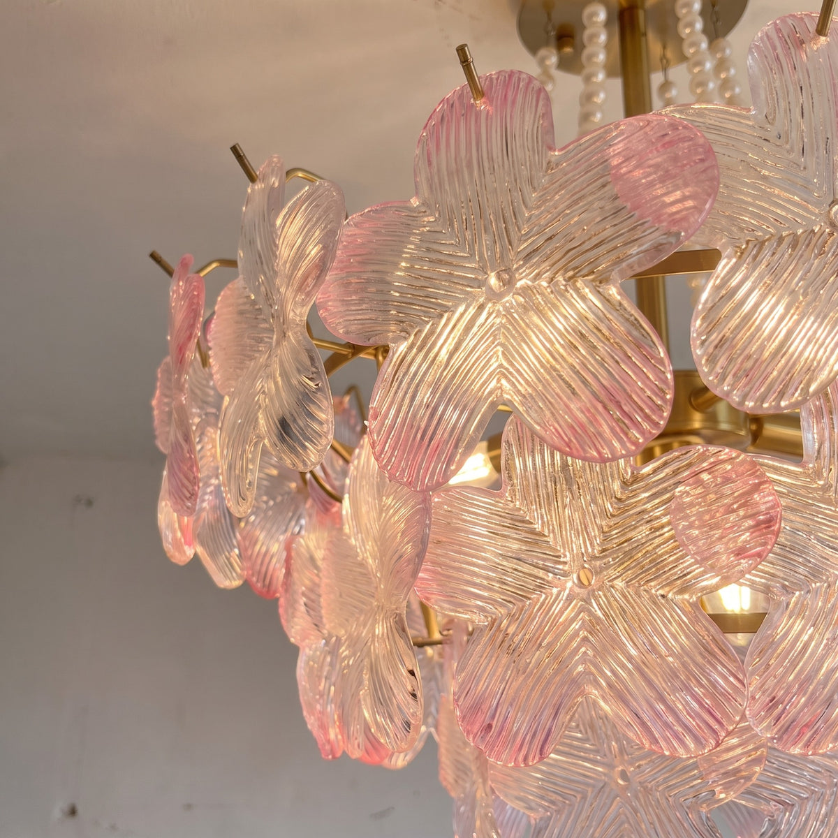Détail rapproché d'un lustre élégant, montrant les pampilles de perles et les délicats pétales de verre rose pastel.