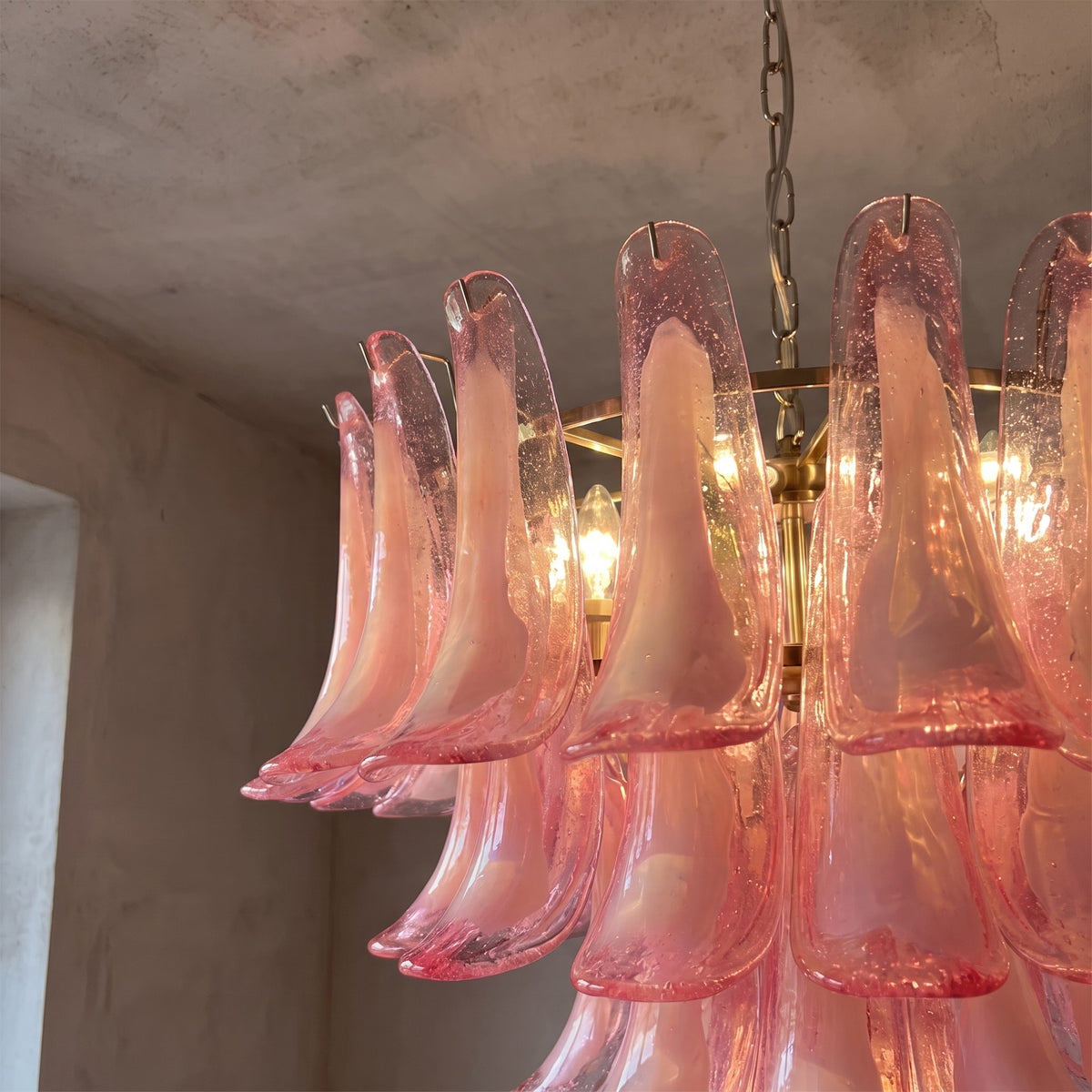 Vue rapprochée d'un lustre rose en verre façonné comme des pétales, illuminant une pièce avec une ambiance douce et raffinée.