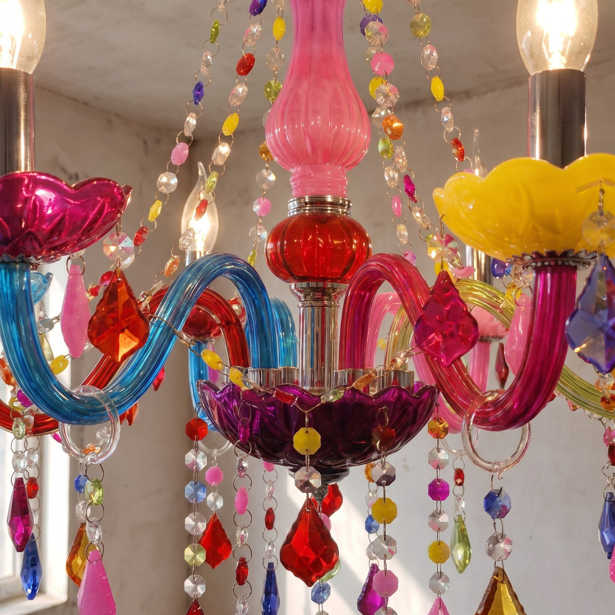 Détail rapproché des bras et coupelles du lustre style Murano, présentant des teintes vives de rose, jaune, bleu et violet. Les cristaux brillent.