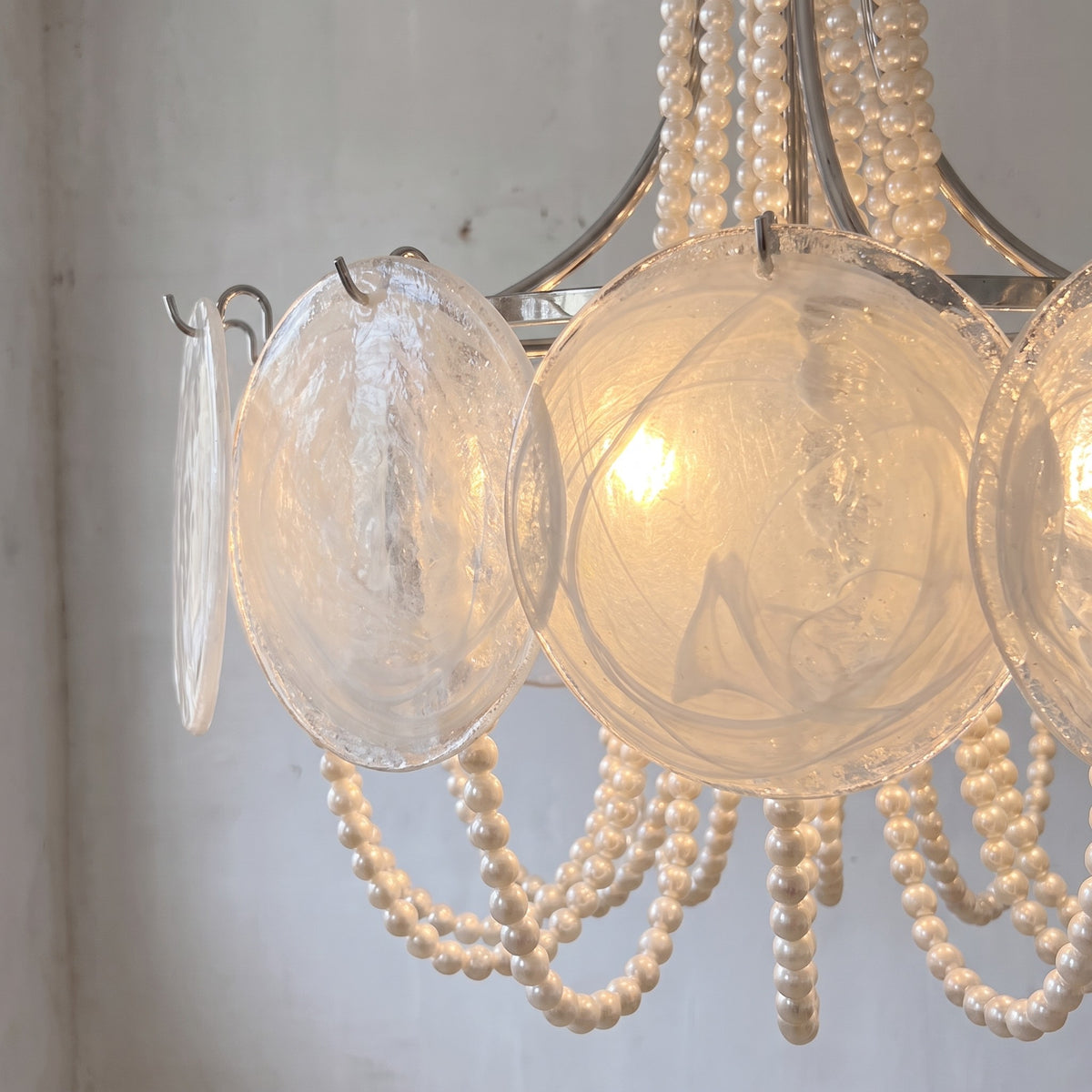 Détail des disques de verre opalin nacré du lustre style Murano, capturant la lumière avec subtilité pour une ambiance chaleureuse.