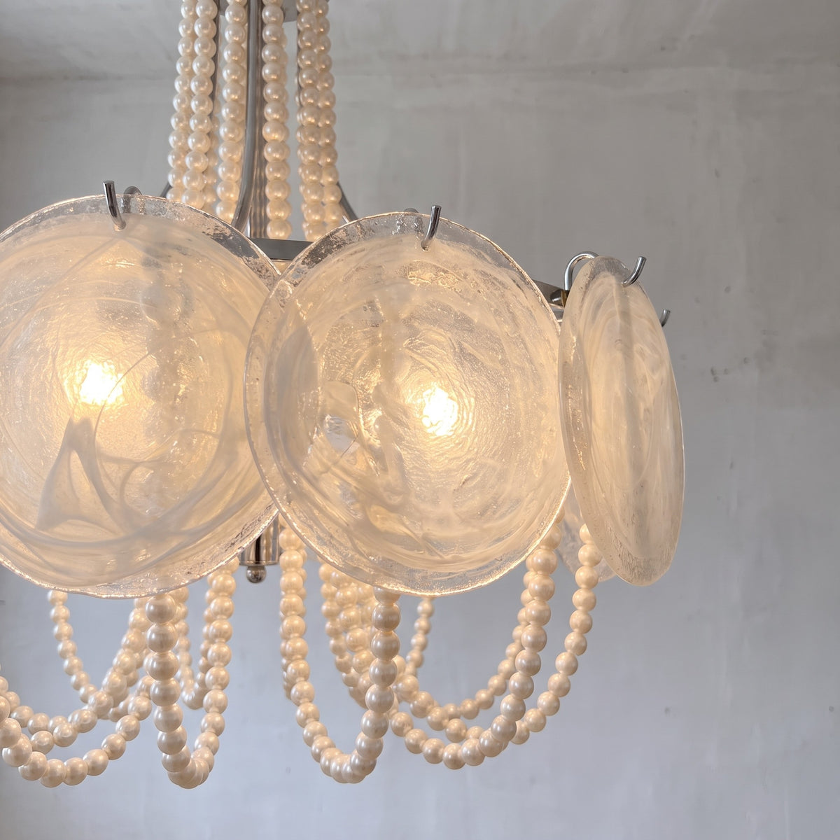 Cascades de perles ivoire délicates suspendues au lustre, ajoutant une texture riche et un mouvement gracieux au luminaire.