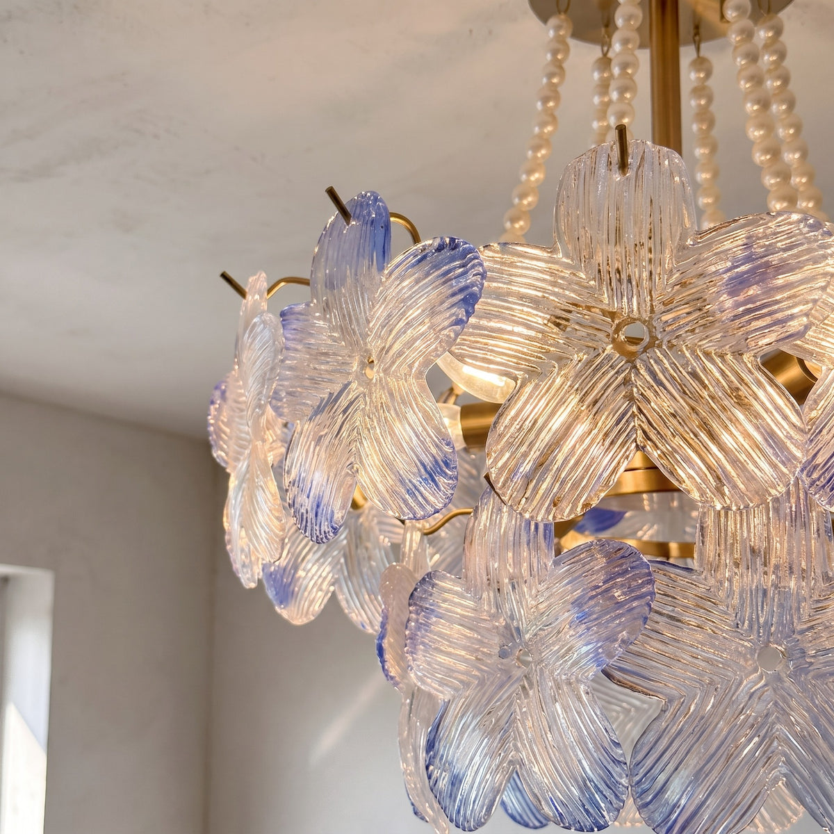 Vue rapprochée des pétales de verre opalescent rose poudré et bleu clair d'un lustre de style Murano, détail artisanal.