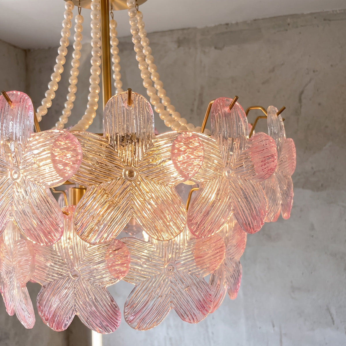 Gros plan sur les pétales de verre rose du lustre, révélant leur texture striée et la subtilité de leur dégradé de couleur.