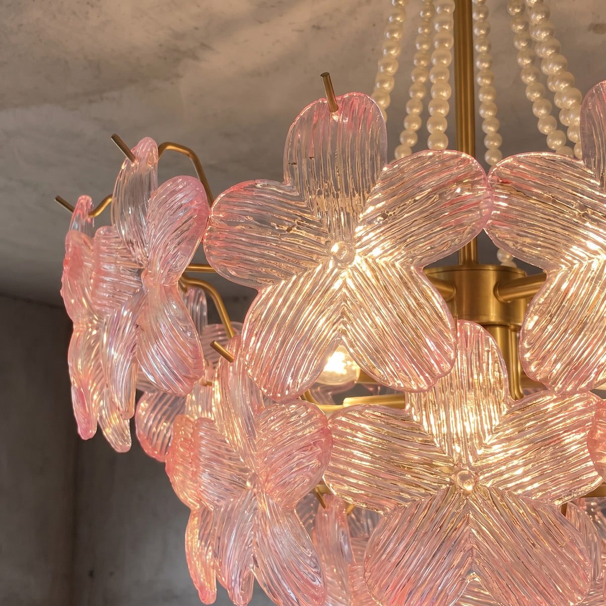 Vue rapprochée du corps du lustre, révélant la fixation au plafond et les chaînes de perles, symbole d'un design sophistiqué.
