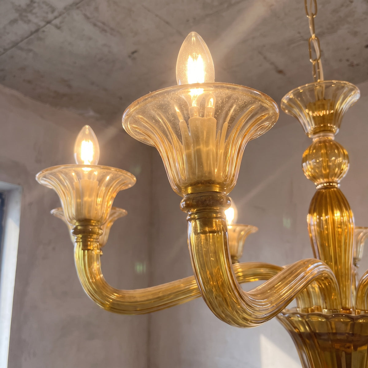 Détail du verre soufflé vert ambré, mettant en valeur les courbes et la texture unique de ce luminaire vénitien, reflet d'un savoir-faire.
