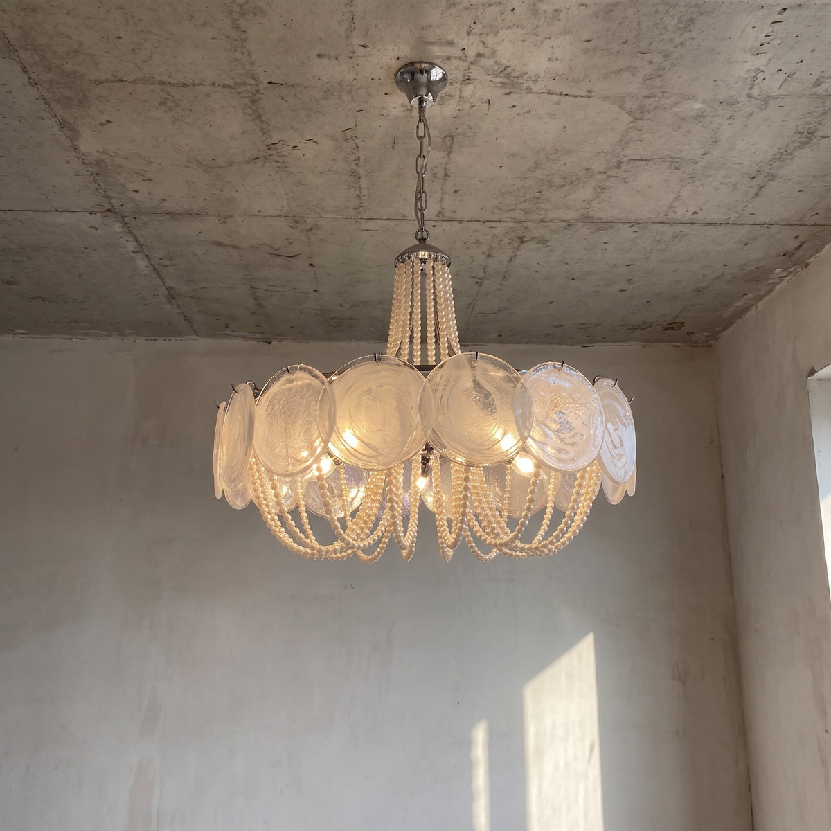 Lustre style Murano rond avec disques en verre irisé et perles suspendues, ambiance lumineuse douce dans un salon élégant.