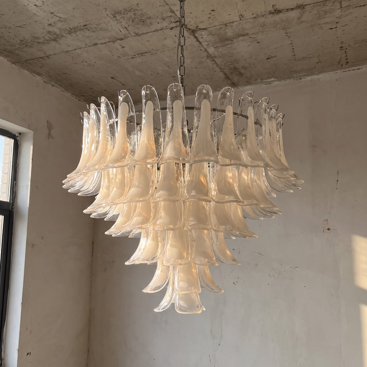 Vue d'ensemble du grand lustre de style Murano en verre blanc opalin, suspendu et illuminé, soulignant sa structure élégante en métal chromé.